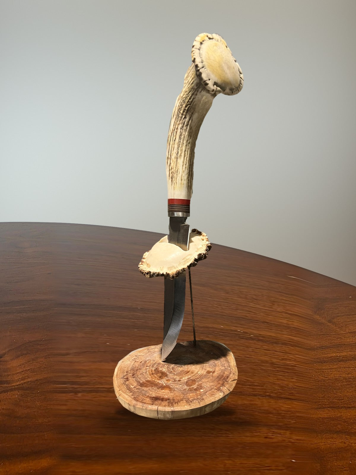Handgefertigtes Messer mit Geweihgriff auf Ständer aus Holzscheibe und Geweihplatte, auf rundem Holztisch
